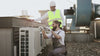 2 men working on a heat pump or air conditioner on the roof of a commercial building