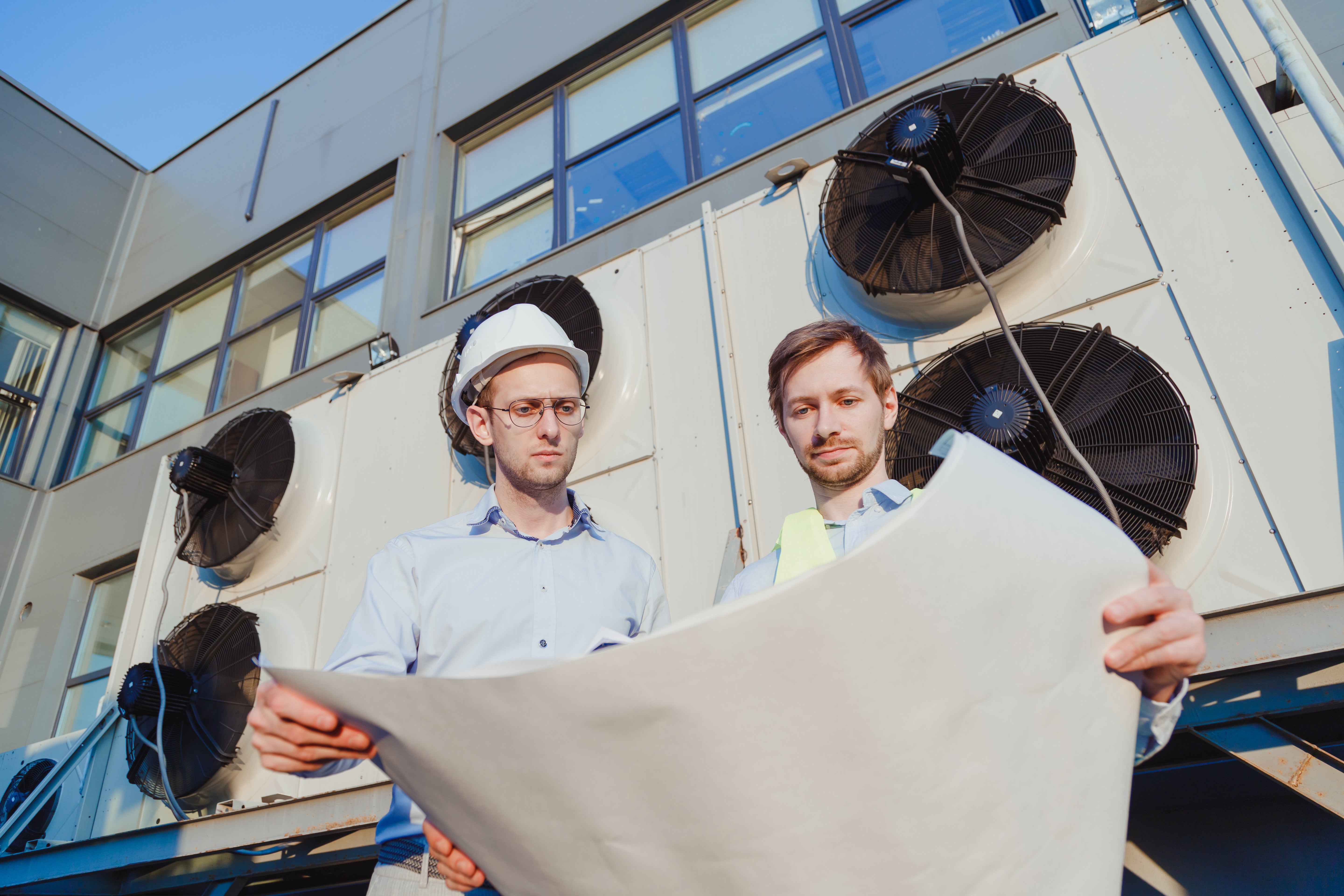 2 men looking at a blueprint next to HVAC units a commercial building