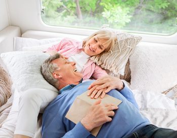 Happy mature woman and her husband relaxing on bed in their motorhome during camping vacation